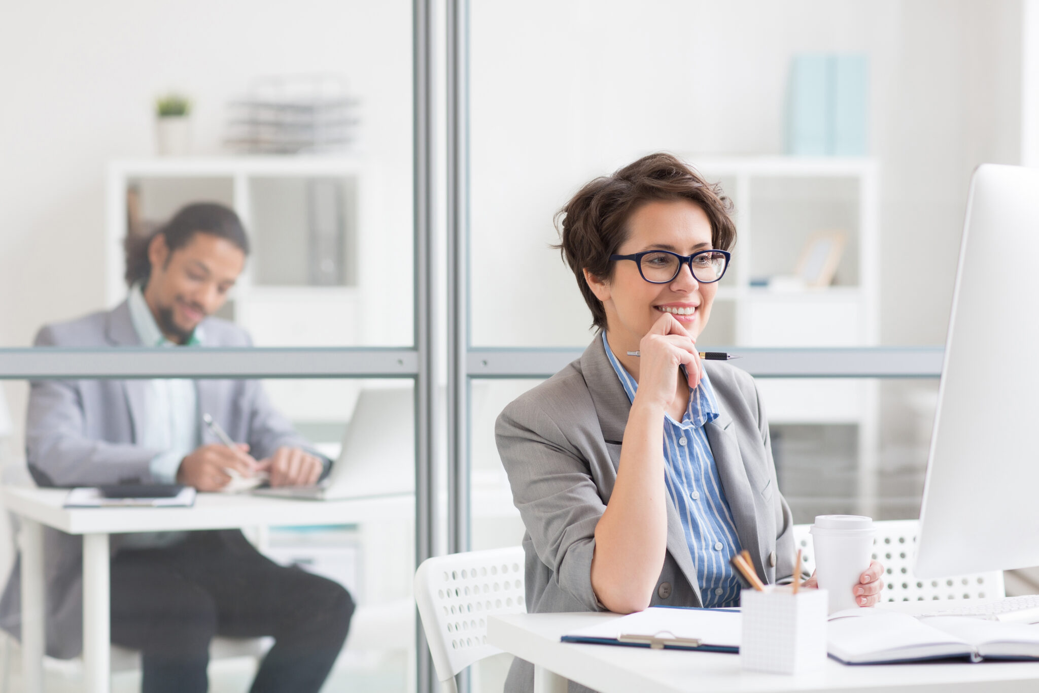 Eine Employer Branding Spezialistin sitzt an einem Schreibtisch in einem hellen Büro und arbeitet konzentriert am Computer. Im Hintergrund ist ein weiterer Kollege an einem Schreibtisch zu sehen.