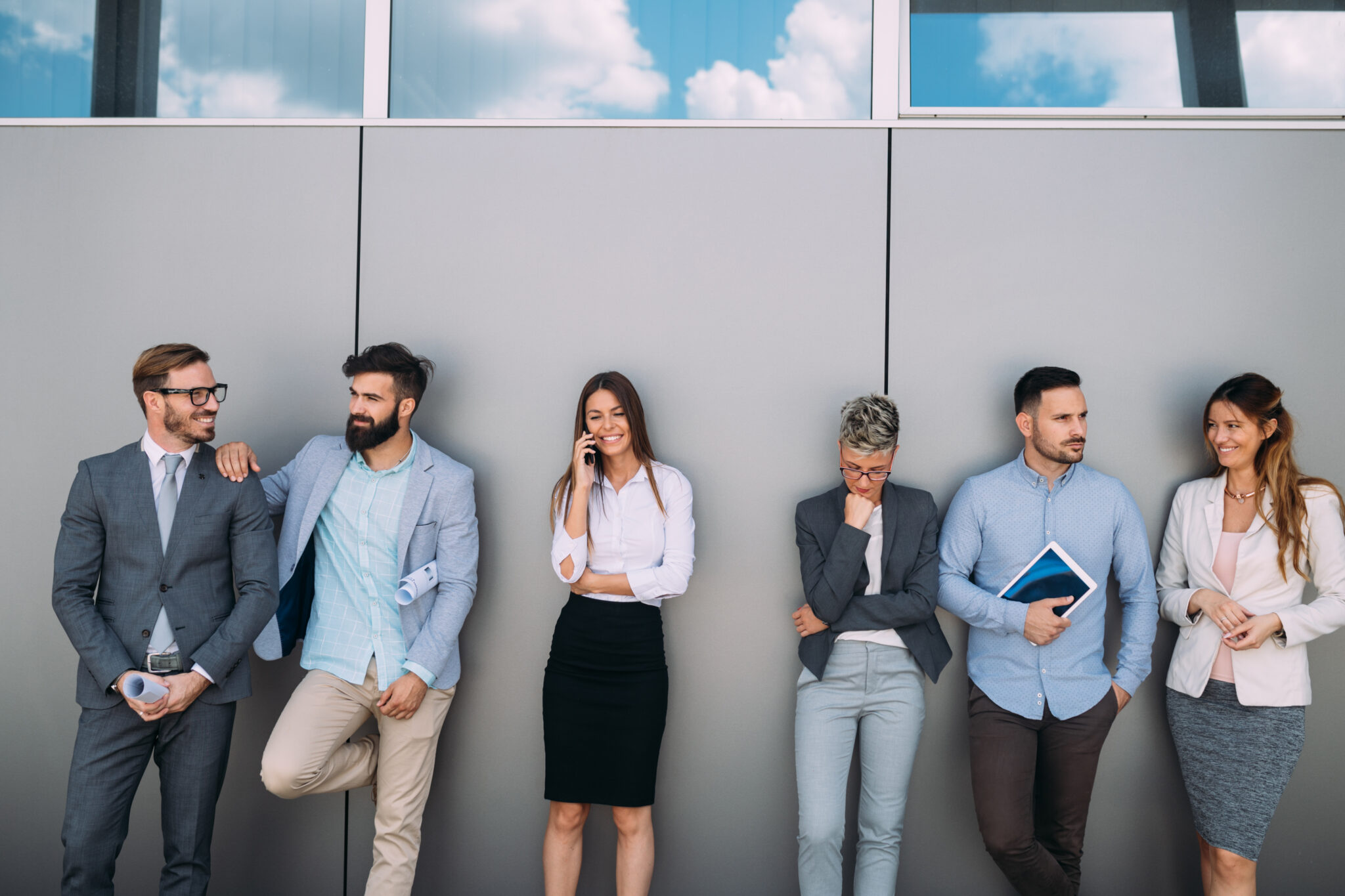 Eine Gruppe von sechs Geschäftspersonen steht lässig vor einer grauen Wand. Sie verkörpern Diversität und Professionalität und symbolisieren die Notwendigkeit, qualifizierte Employer Branding Experten sorgfältig auszuwählen.