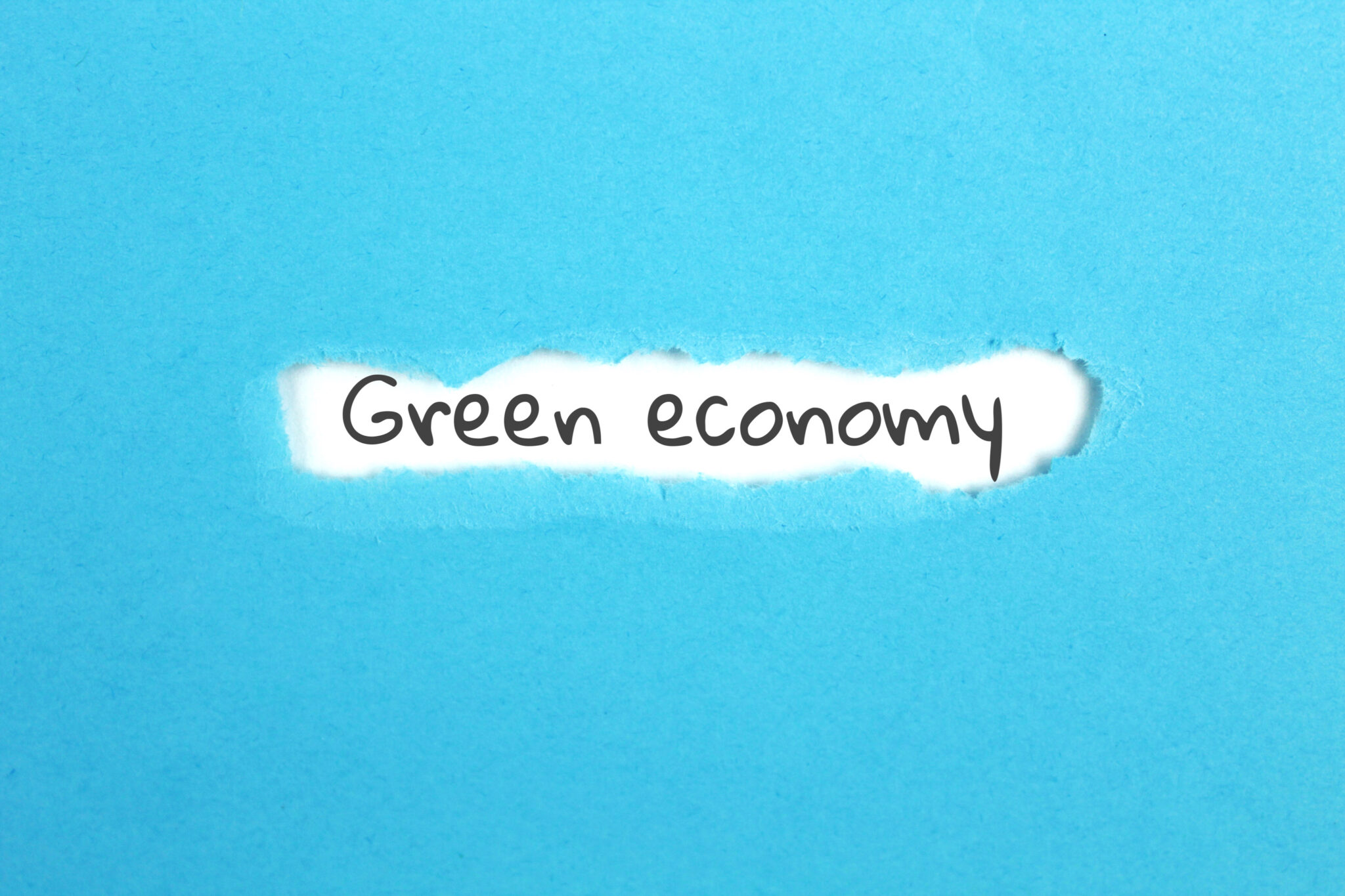 Nahaufnahme eines blauen Blattes Papier, in dem ein Riss die Worte ‚Green economy‘ in schwarzer Handschrift