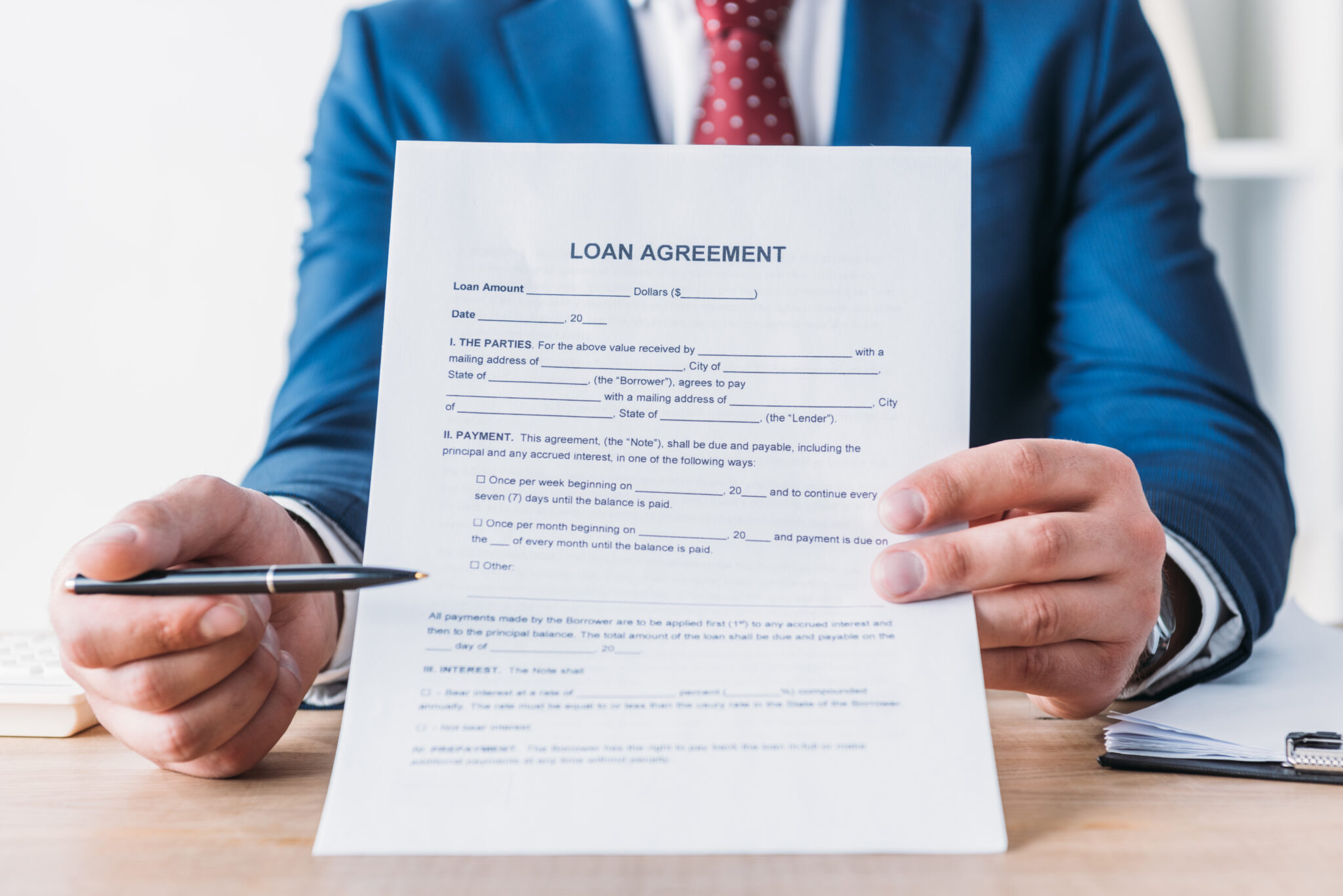 Eine Person in einem Anzug hält ein Dokument mit der Überschrift 'Loan Agreement' (Darlehensvertrag) und zeigt mit einem Stift darauf. Das Bild verdeutlicht, dass ohne die Zustimmung der Marktfolge kein Kredit vergeben wird. Das Dokument und die Gestik symbolisieren die Wichtigkeit der formalen Genehmigung im Kreditvergabeverfahren.