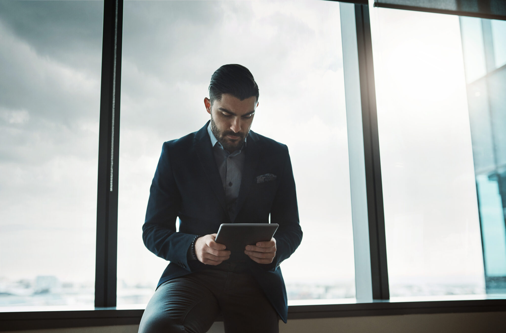 Ein CEO in einem modernen Büro, der konzentriert auf ein Tablet schaut, was technologisches Verständnis und digitale Kompetenz symbolisiert.