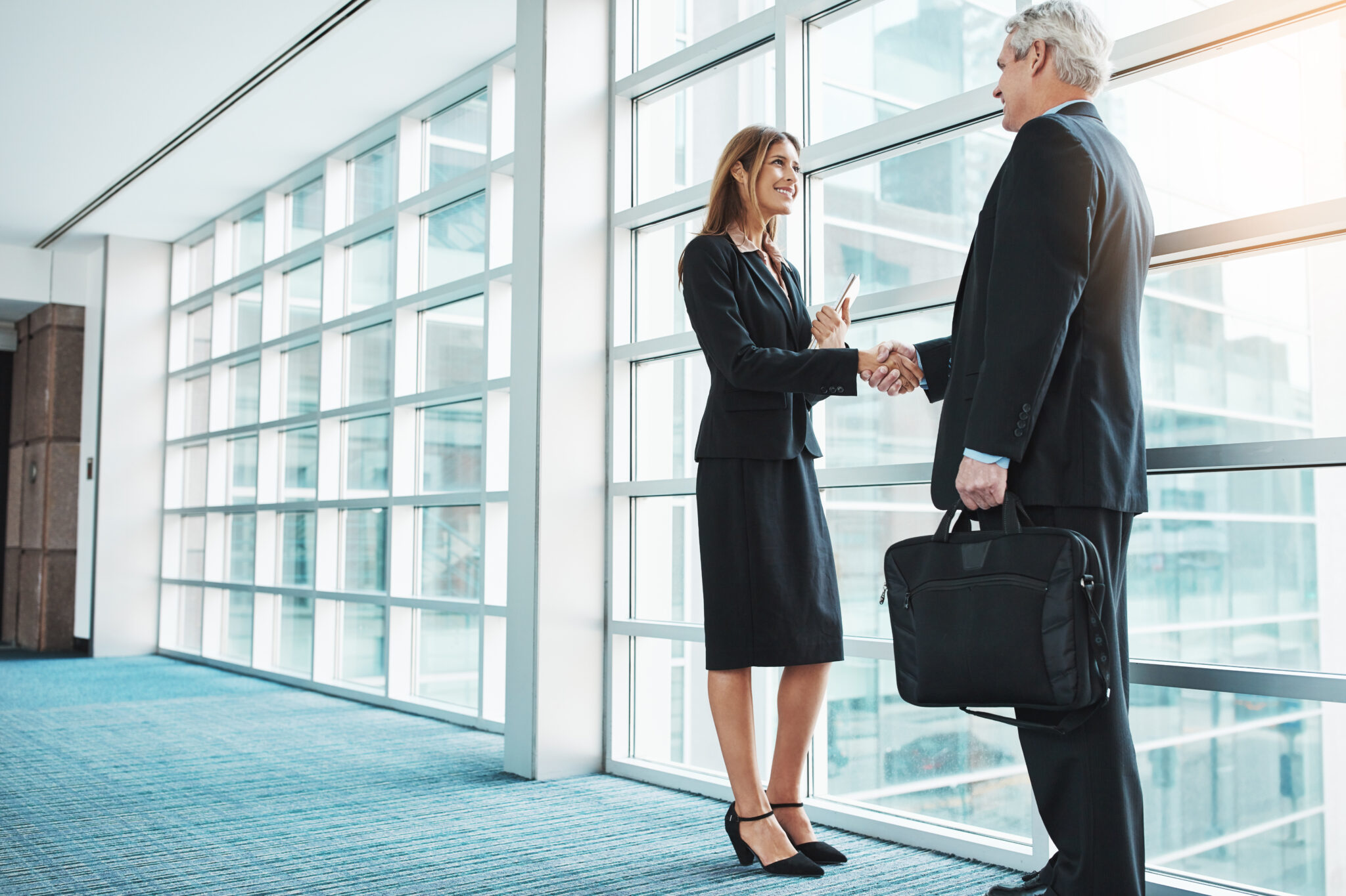 Ein CEO und eine Geschäftspartnerin in einem modernen Bürogebäude beim Händeschütteln, symbolisierend die Bedeutung von Netzwerken und Beziehungsmanagement.