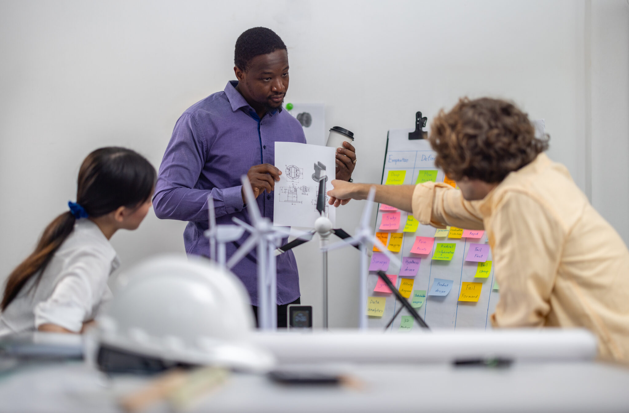 Fotografie eines Teams in einem technologiegetriebenen Unternehmen, das an Produktentwicklungsplänen arbeitet; ein CTO präsentiert Entwürfe, während ein agiles Board mit Post-its im Hintergrund den Entwicklungsprozess unterstützt.