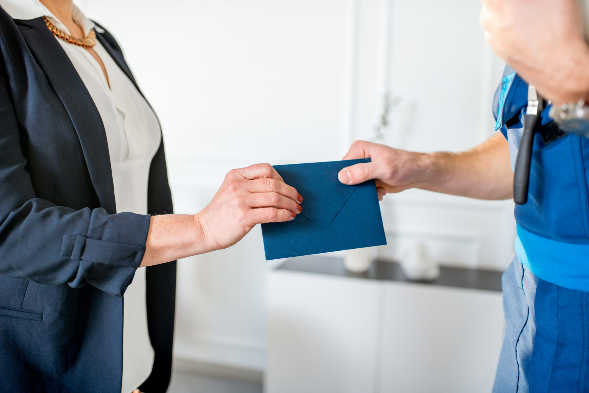 Frau im Business-Outfit überreicht einem Handwerker das Gehalt in einem Umschlag.