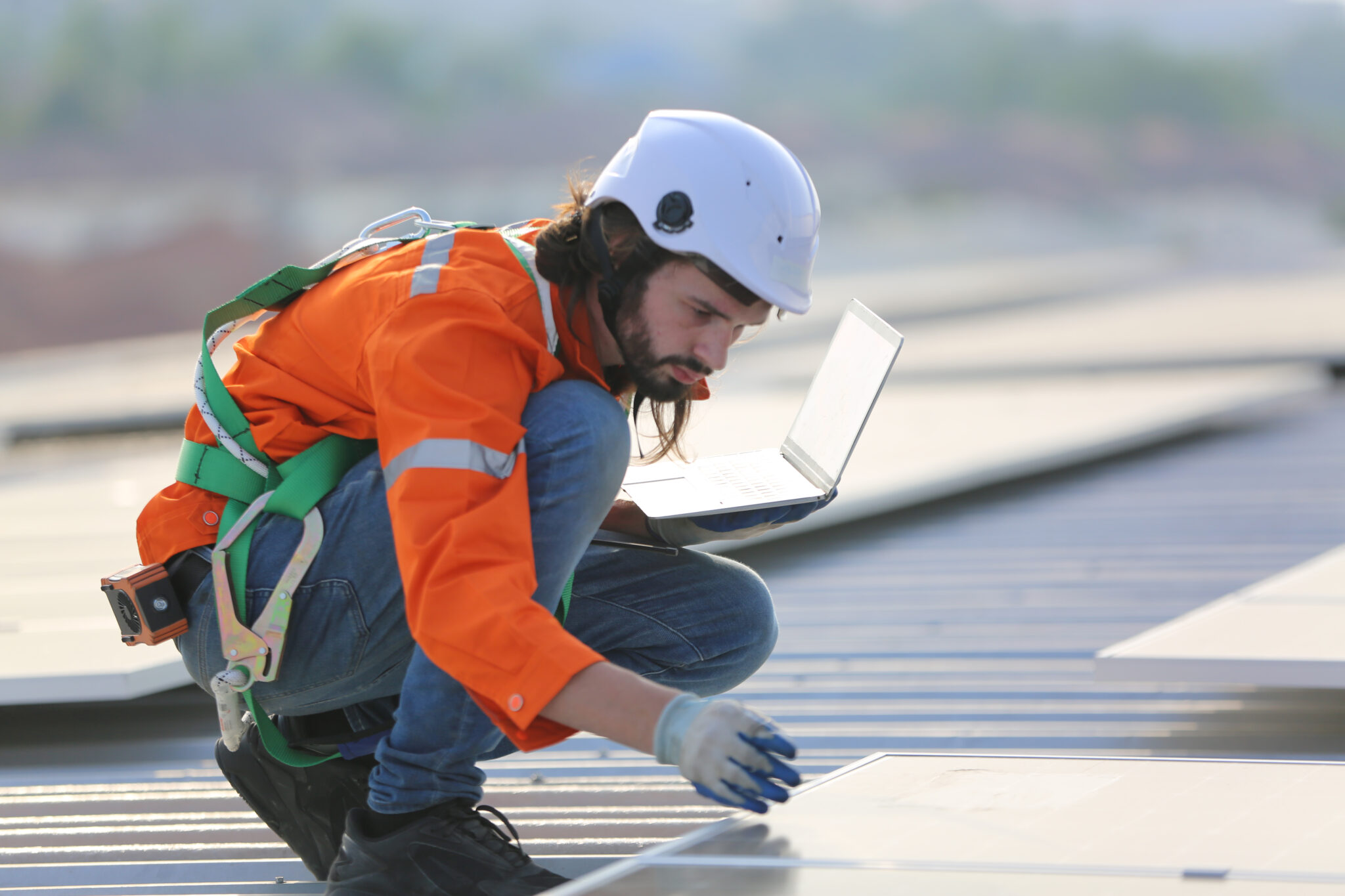 Ein junger Techniker in Schutzkleidung und Helm arbeitet auf einem Solarpanel-Dach. Er trägt einen Sicherheitsgurt und verwendet einen Laptop, um Daten zu überprüfen oder Einstellungen vorzunehmen. Der Untertitel „Nachwuchs kann die Lücke durch abgehende Babyboomer nicht schließen“ betont die Herausforderungen bei der Sicherstellung einer ausreichenden Fachkräftebasis in der Energiebranche. Die Szene symbolisiert die Verbindung von technischer Arbeit und moderner Technologie im Bereich erneuerbarer Energien.