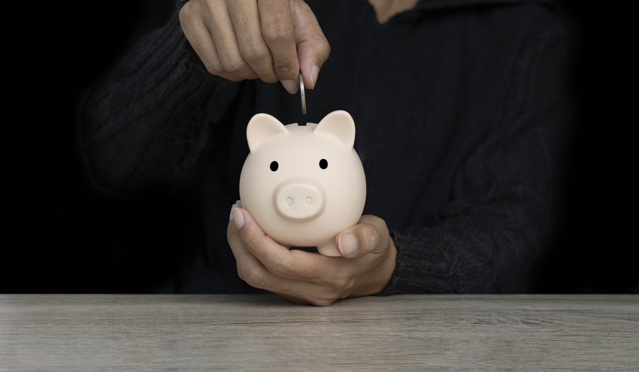 Person legt eine Münze in ein Sparschwein, symbolisiert Kosteneinsparungen durch reduzierte Bürofläche bei Remote-Arbeit und Homeoffice.