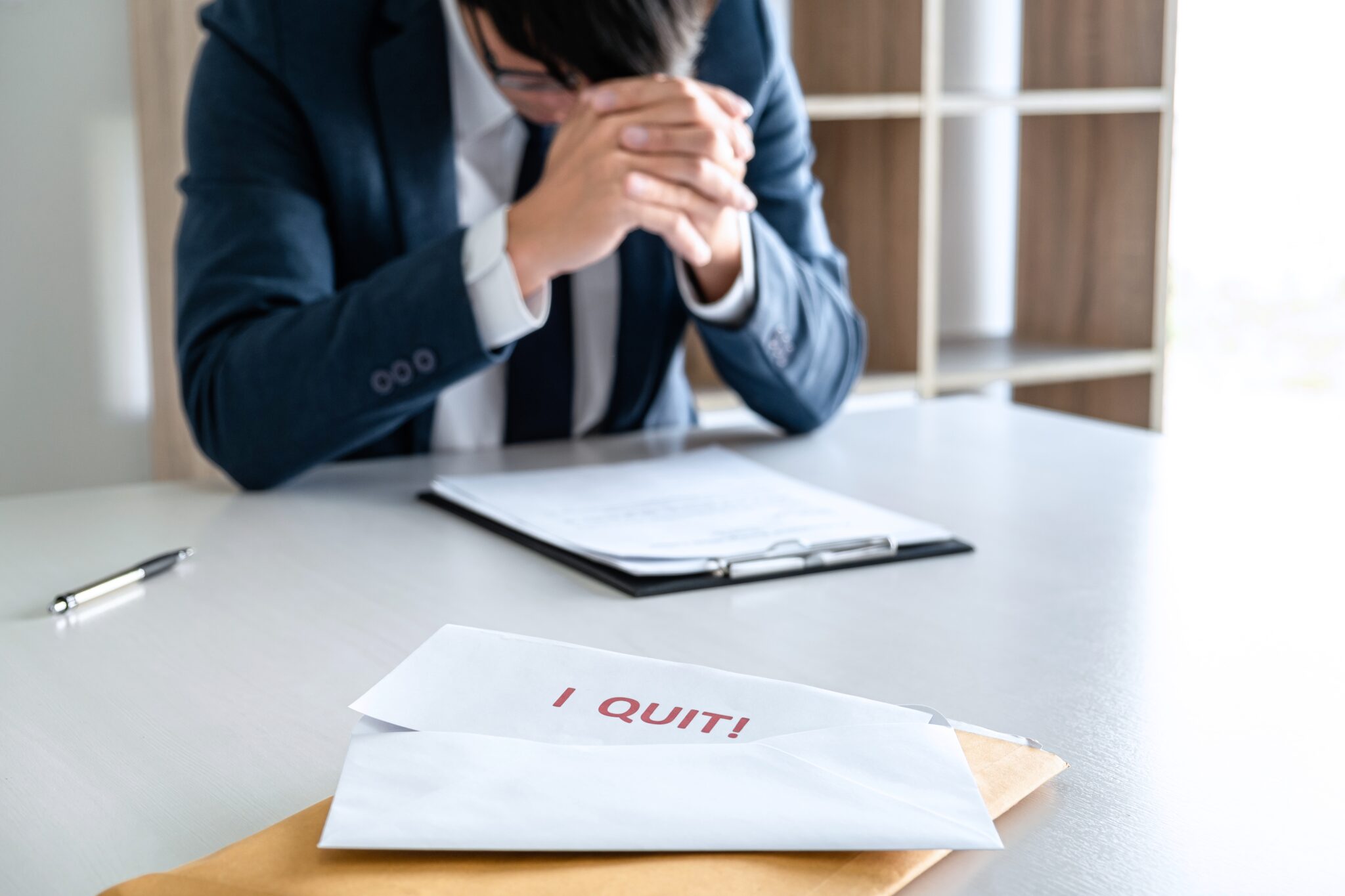 Viele Arbeitnehmer sind unzufrieden Ein Angestellter sitzt nachdenklich am Schreibtisch mit einem Kündigungsschreiben, auf dem 'I QUIT!' steht, im Vordergrund. Symbolisiert die Unzufriedenheit vieler Arbeitnehmer (Stichwort: Quiet Quitting).