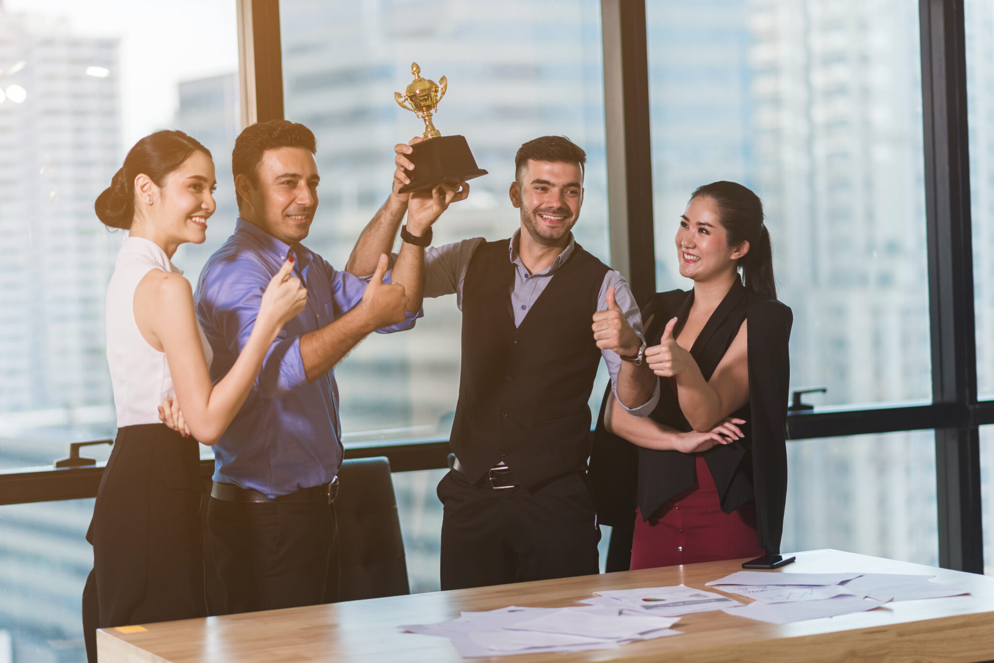 Eine Gruppe von vier IT-Fachkräften in einem modernen Büro, die gemeinsam einen Pokal hochhalten und lächeln. Zwei Personen zeigen mit Daumen hoch.