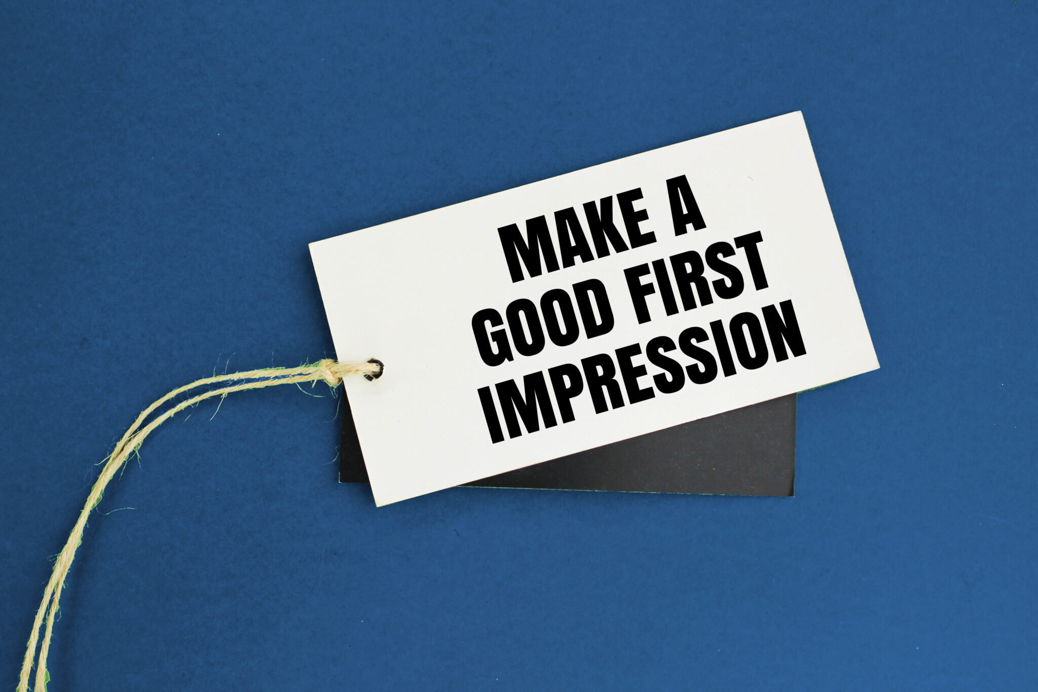 Ein Etikett mit der Aufschrift "Make a good first impression" liegt auf blauem Hintergrund. Dieses Bild symbolisiert die Bedeutung eines positiven ersten Eindrucks. Personalberater in Frankfurt unterstützen Unternehmen dabei, sowohl online als auch offline, den richtigen Eindruck zu hinterlassen.