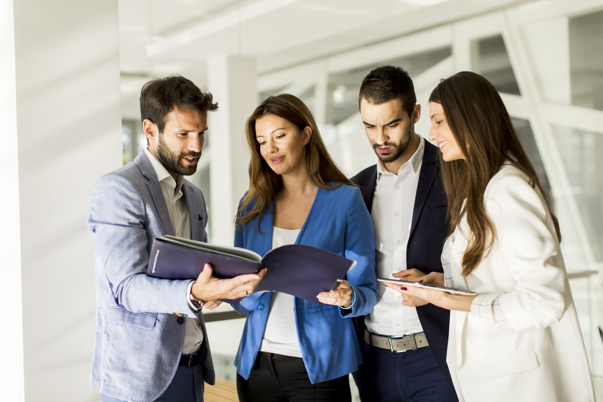 Eine Gruppe bestehend aus zwei Personalberatern und zwei Sparkassenangestellter diskutiert Dokumente in einem modernen Büro. Zwei Männer und zwei Frauen schauen gemeinsam auf Unterlagen, was die sorgfältige Analyse und das Verständnis spezifischer Anforderungen symbolisiert.