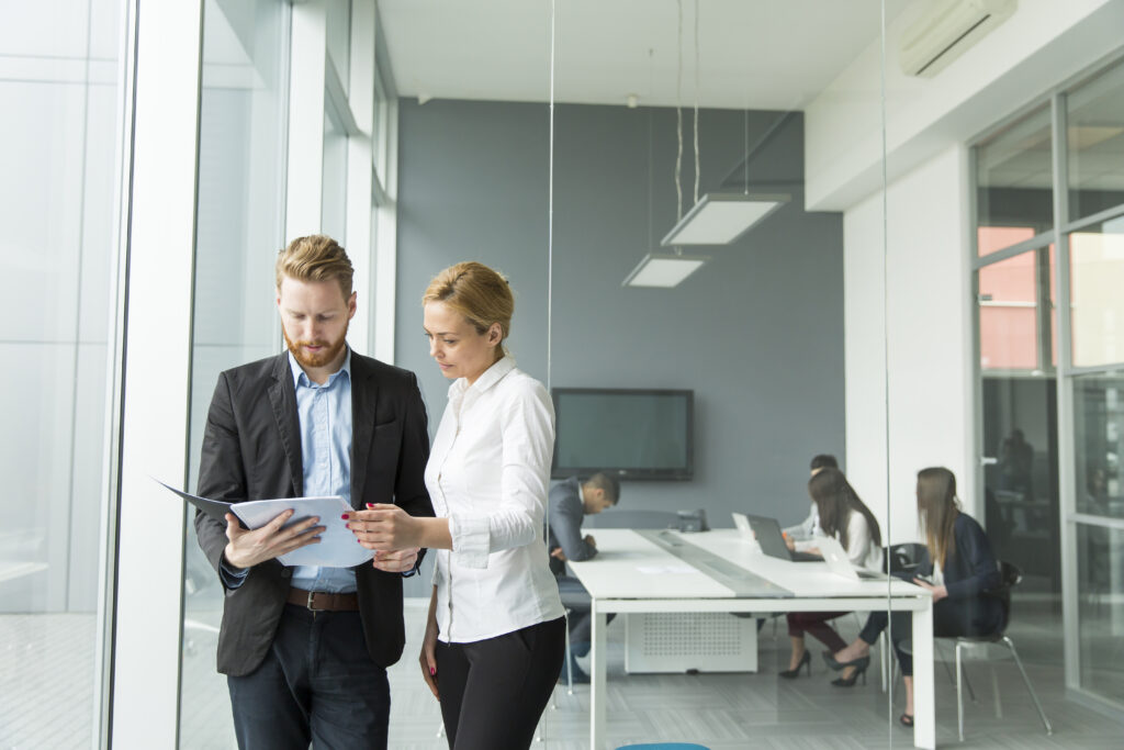 Assistenz der Geschaeftsfuehrung in Business-Kleidung in einem modernen Büro mit Glastüren.