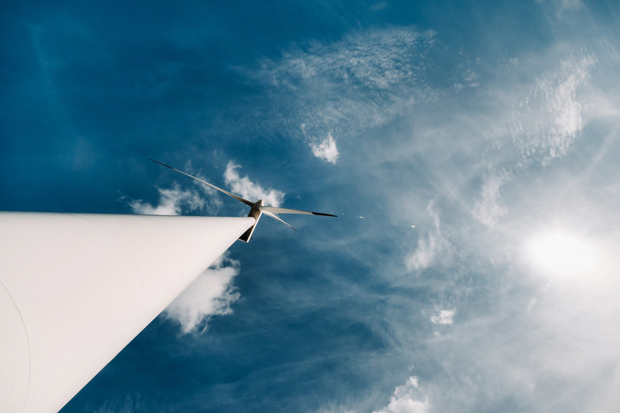 Windrad vor blauem Himmel mit Sonne und Wolken aus der Froschperspektive fotografiert.