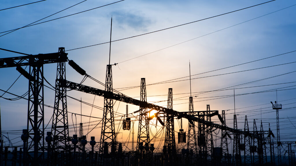 Das Bild zeigt eine elektrische Umspannanlage mit Hochspannungsleitungen vor Sonnenuntergang.