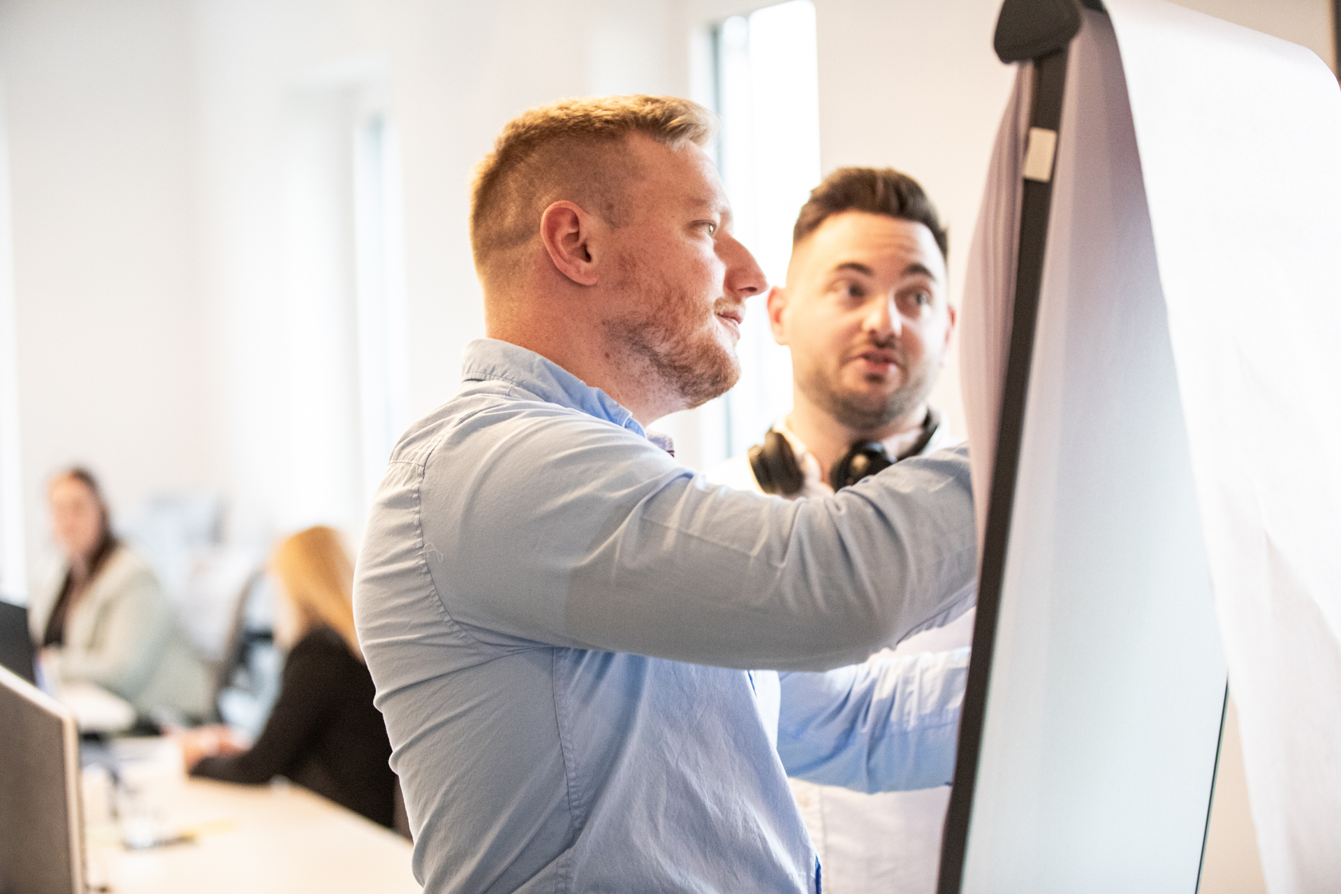 Zwei auf die Bauwirtschaft spezialisierte Personalberater diskutieren vor einem Whiteboard in einem modernen Büroraum.