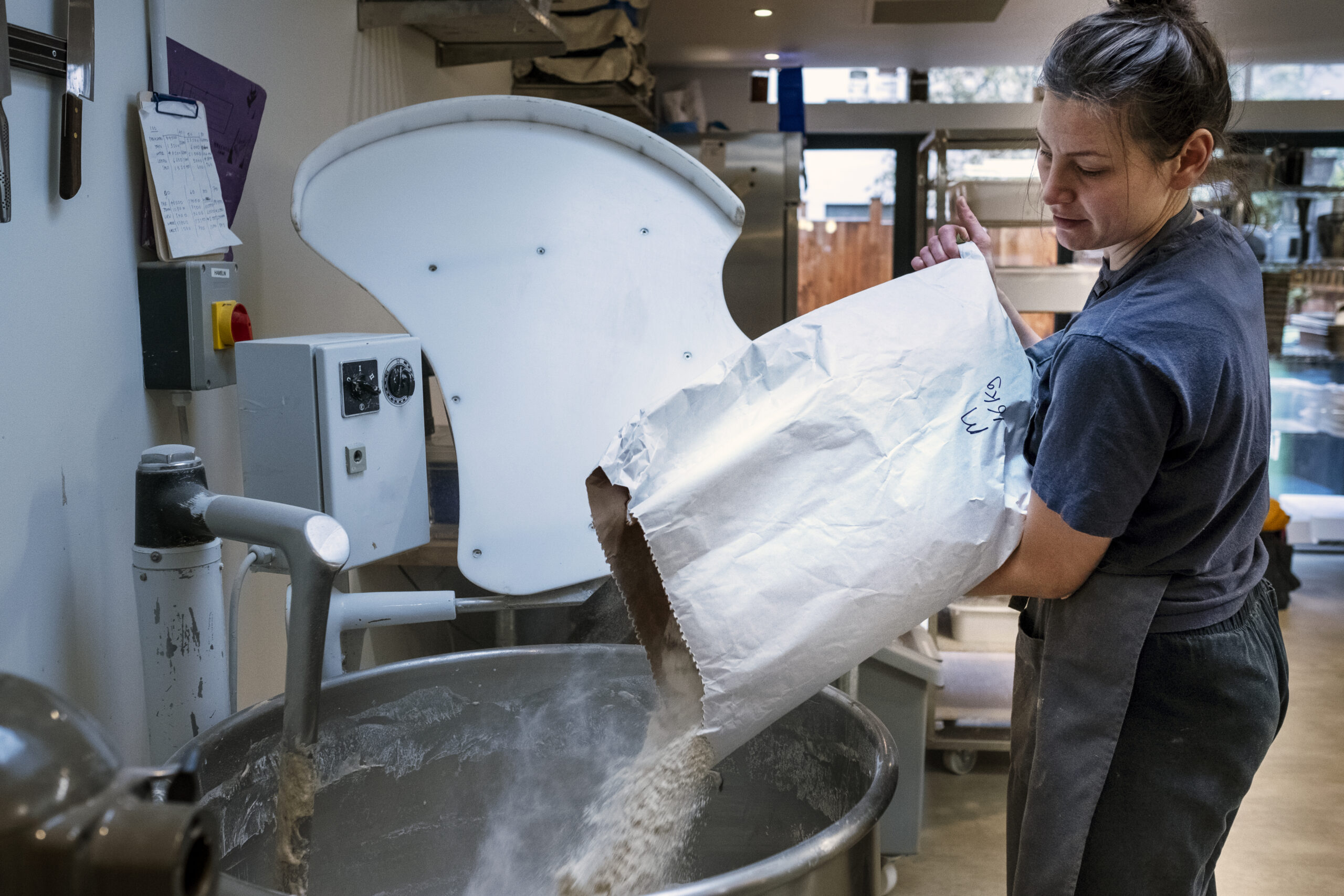 Bäckerin füllt Mehl in Teigknetmaschine. Handwerk in bayerischer Lebensmittelindustrie.