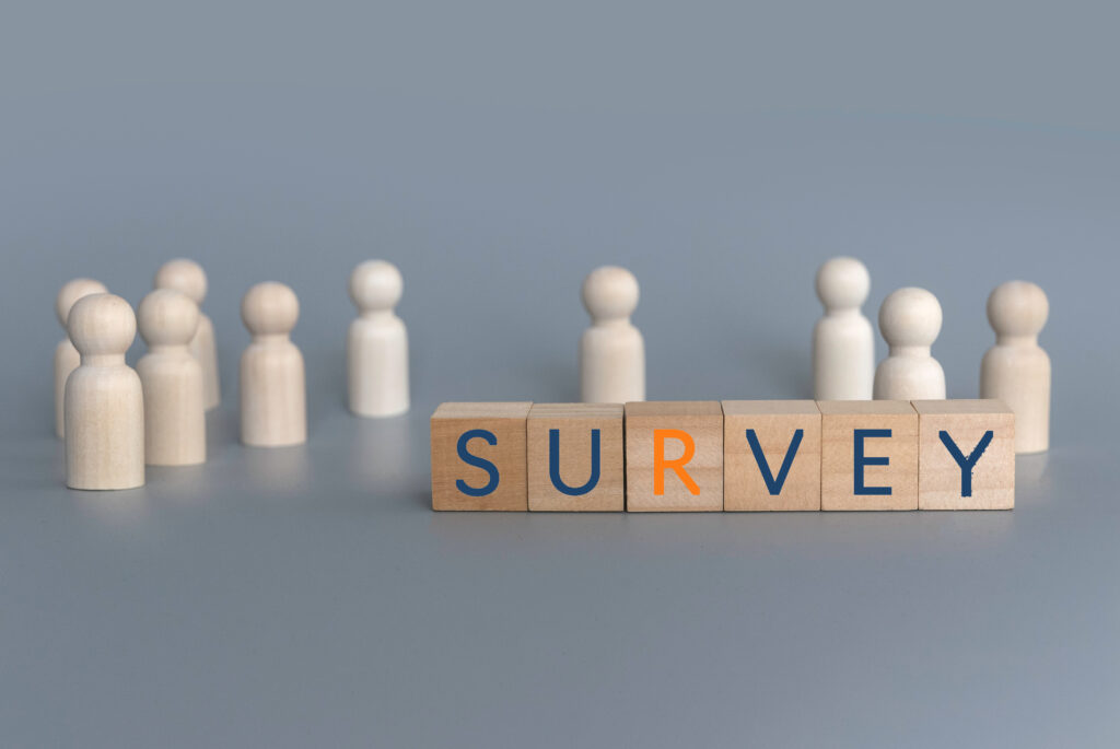 Holzfiguren umgeben Holzklötze mit dem Wort "SURVEY" (Mitarbeiterbefragung Symbolbild)