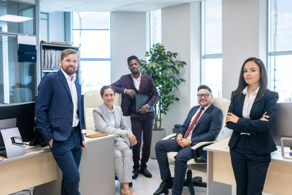 Vier Personen in Business-Kleidung in einem modernen Büro lächeln in die Kamera.