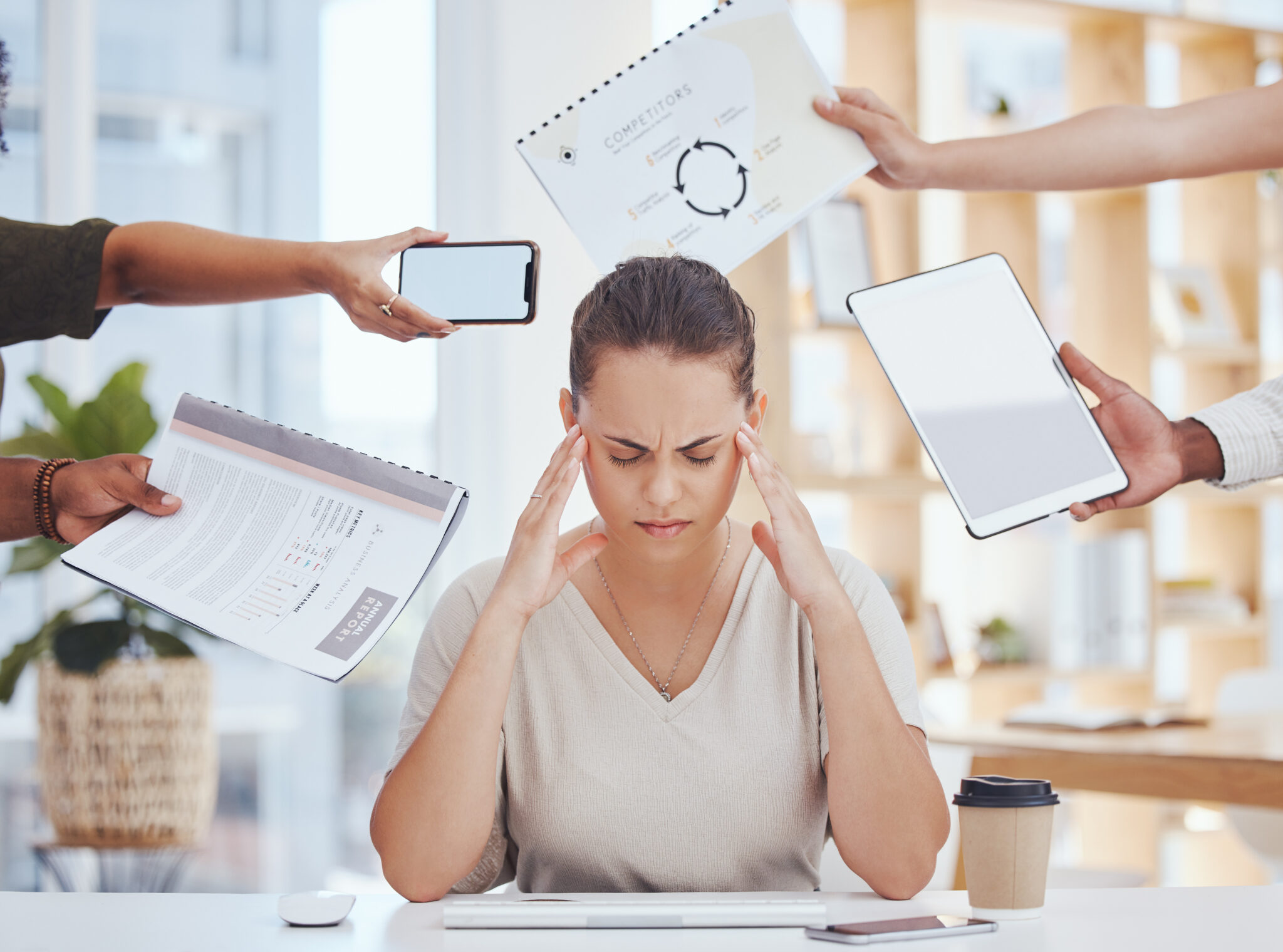 Gestresste HR-Mitarbeiterin am Schreibtisch, umgeben von Papier, Laptop, Tablet und Telefon (Foto)