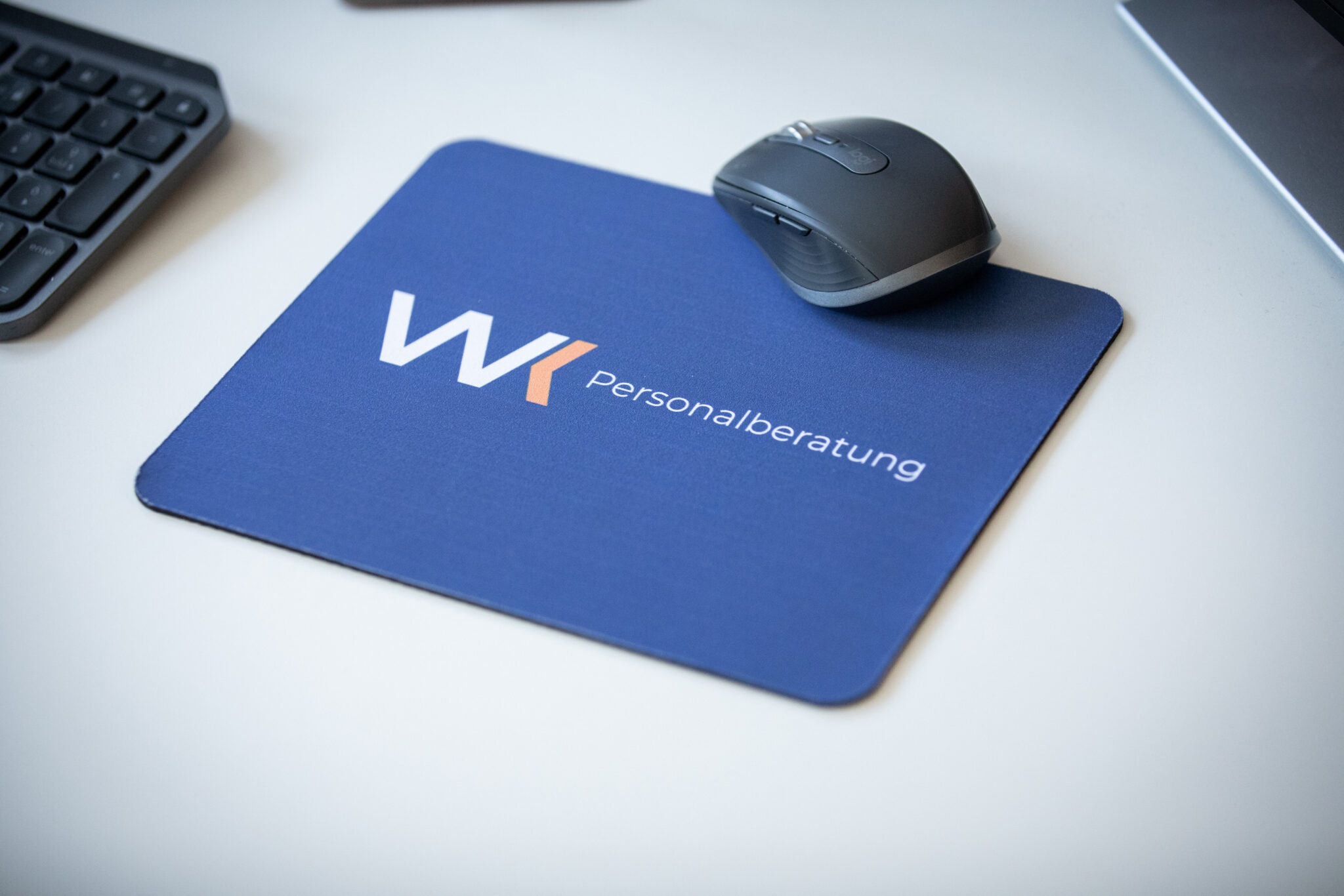 Nahaufnahme: Mauspad mit Logo "WK Personalberatung" und Computermaus auf weißem Schreibtisch.